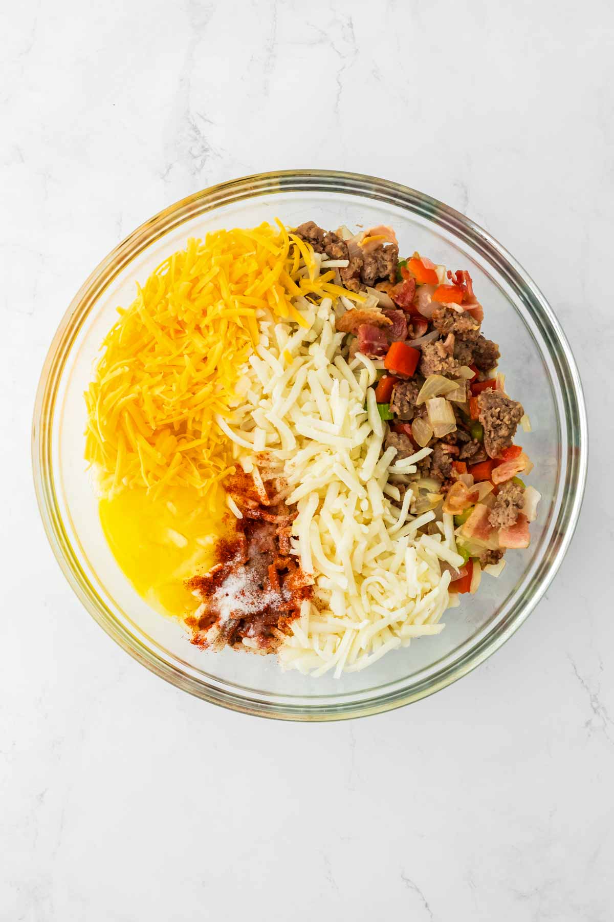 overhead view of sausage and vegetable mixture with cheese and eggs in glass bowl