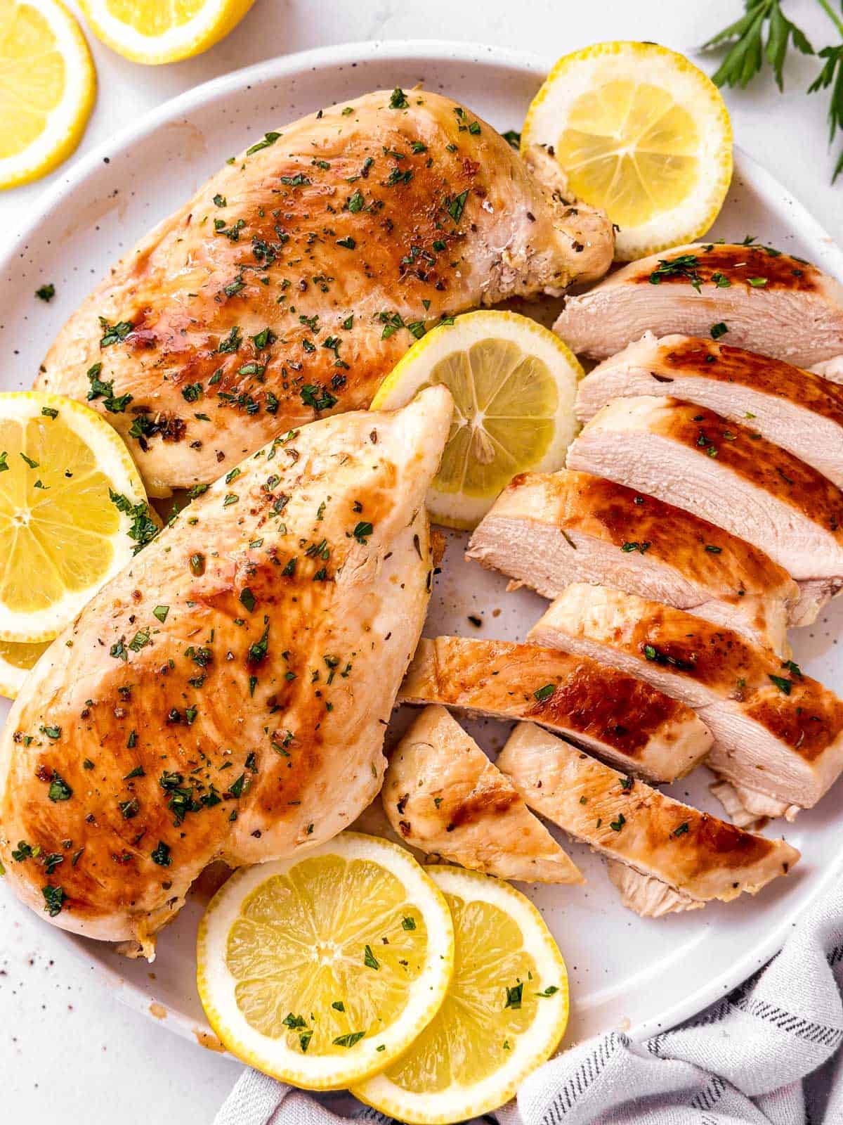overhead view of marinated grilled chicken on white plate with lemon slices