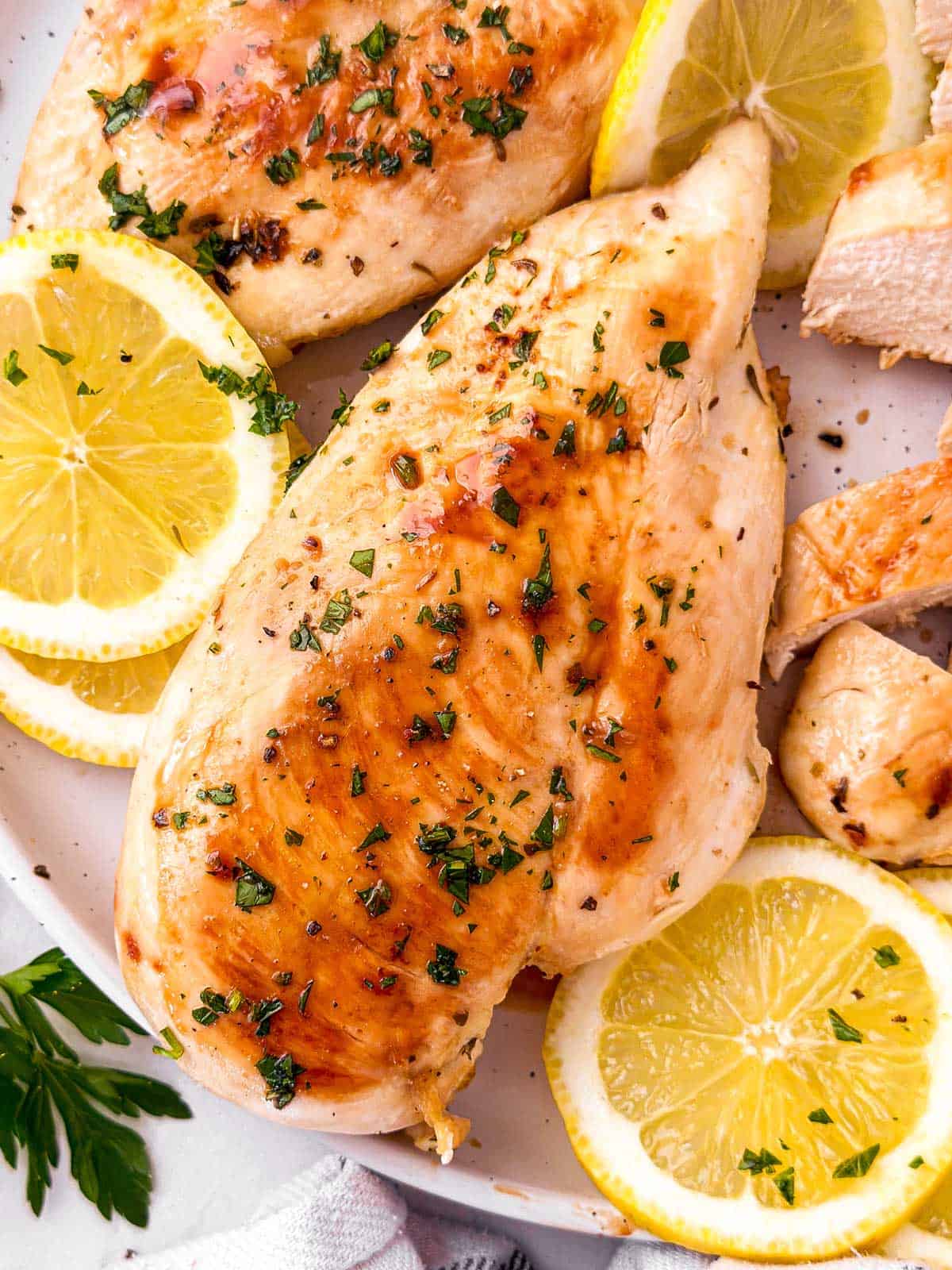 grilled chicken breast on white plate with lemons and parsley