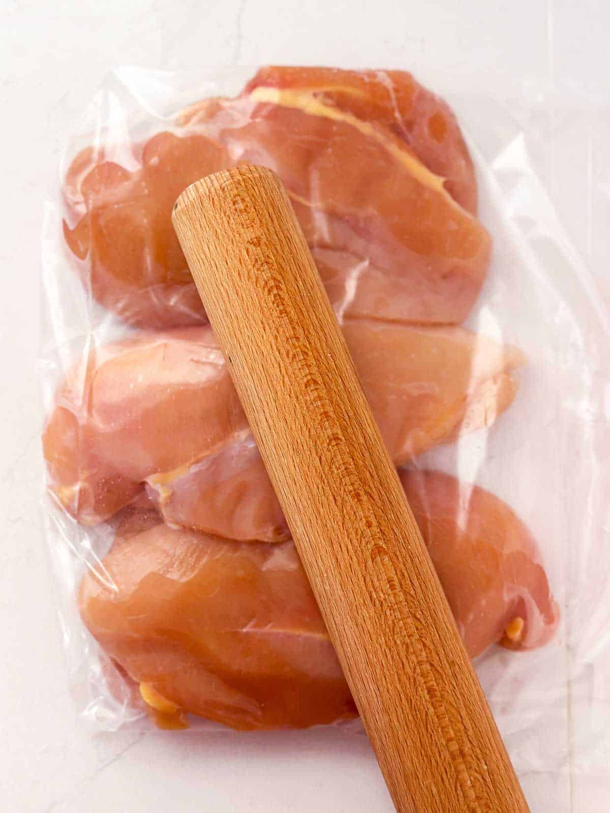 rolling pin on top of chicken breast in ziptop bag
