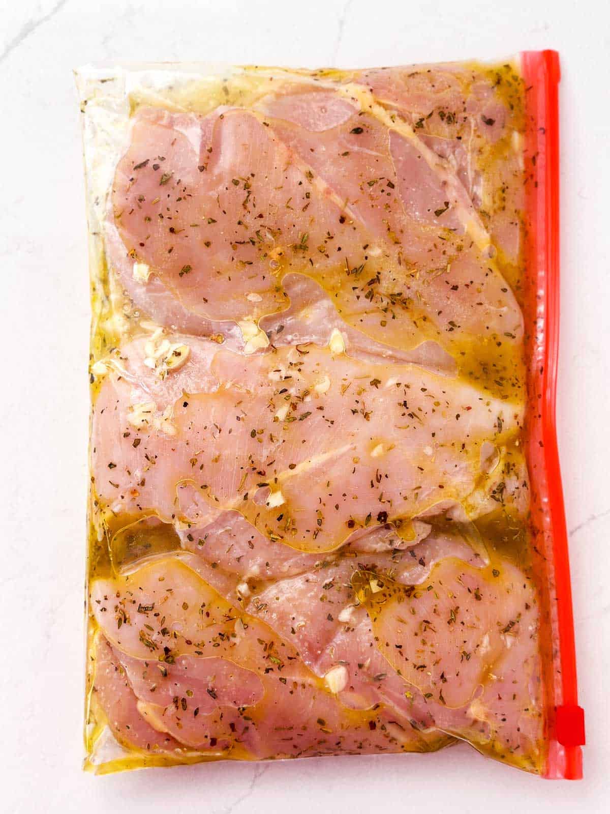 three raw chicken breasts in ziptop bag with lemon garlic marinade