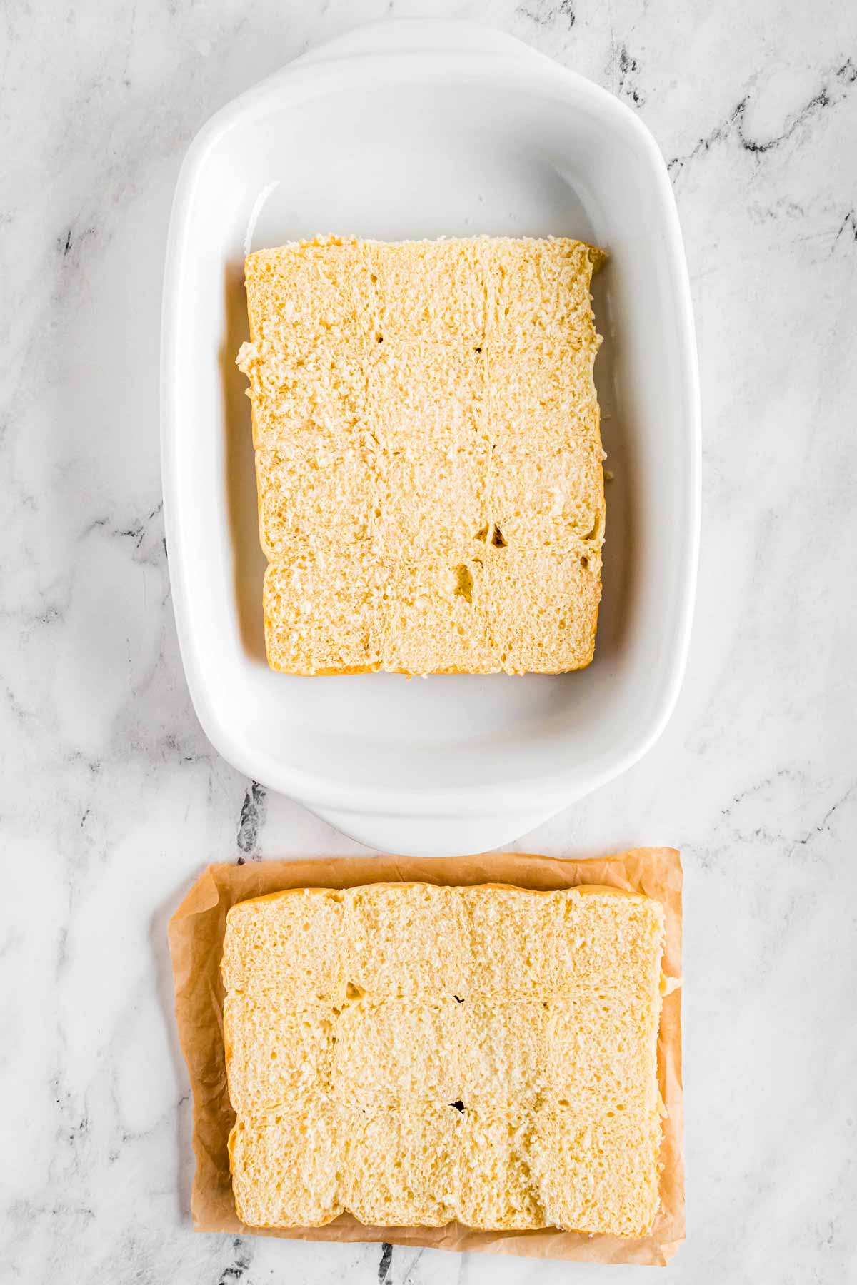 overhead view of slab of dinner rolls cut in half in white baking dish with top half next to it