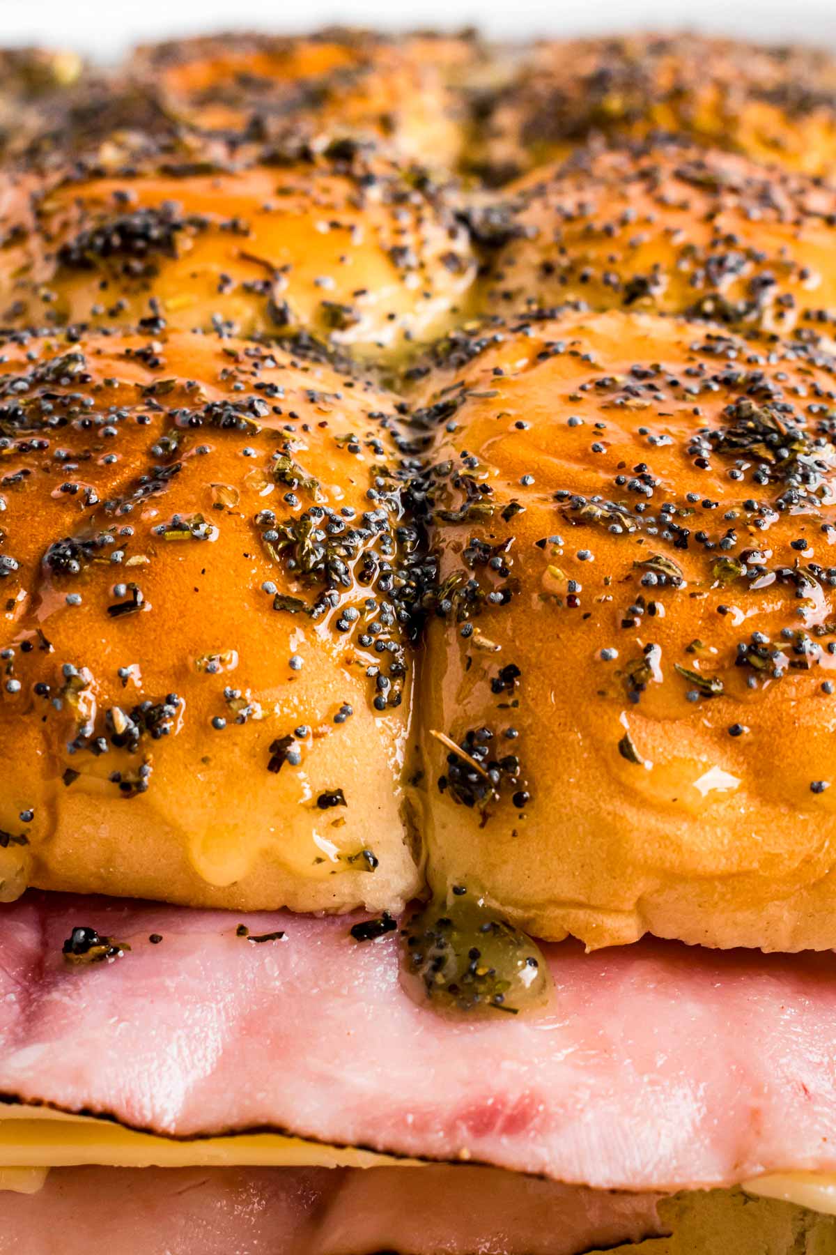 frontal close up of unbaked ham sliders brushed with garlic herb butter