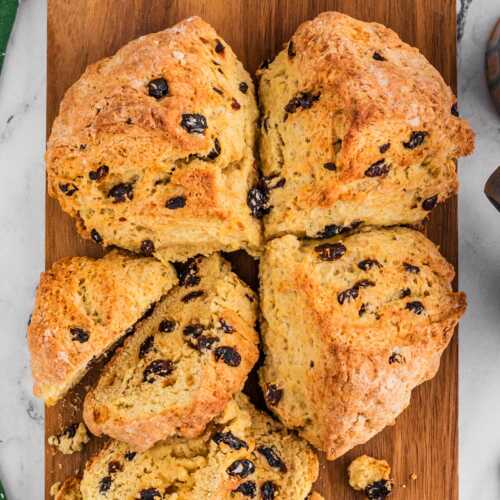 overhead view of Irish soda bread with raisins on wooden board with one quarter removed