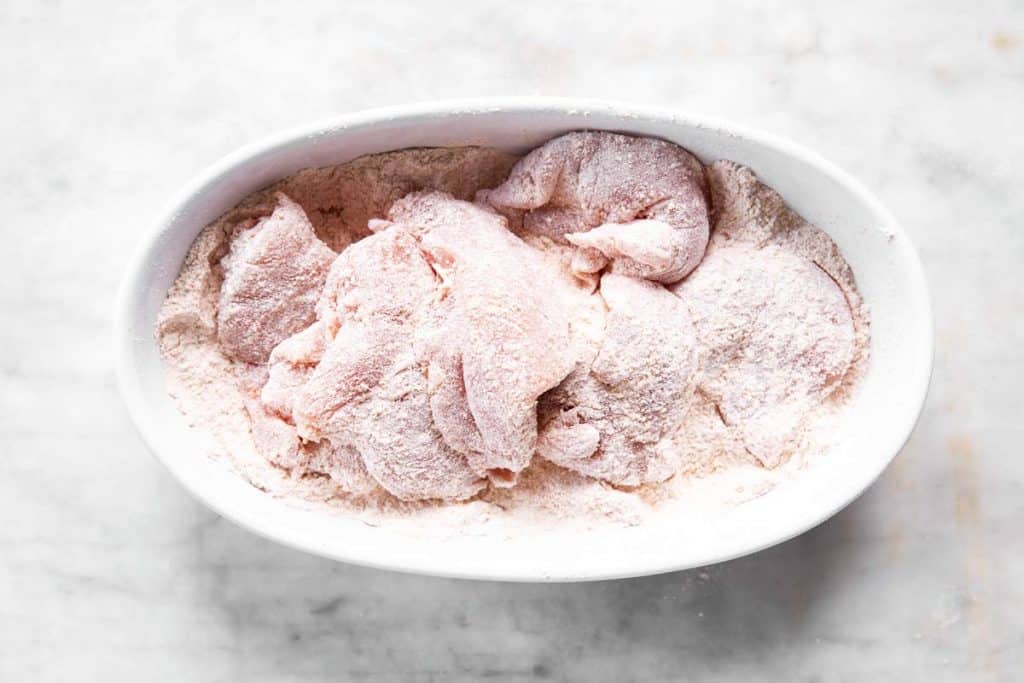 pile of chicken breast in white dish with flour