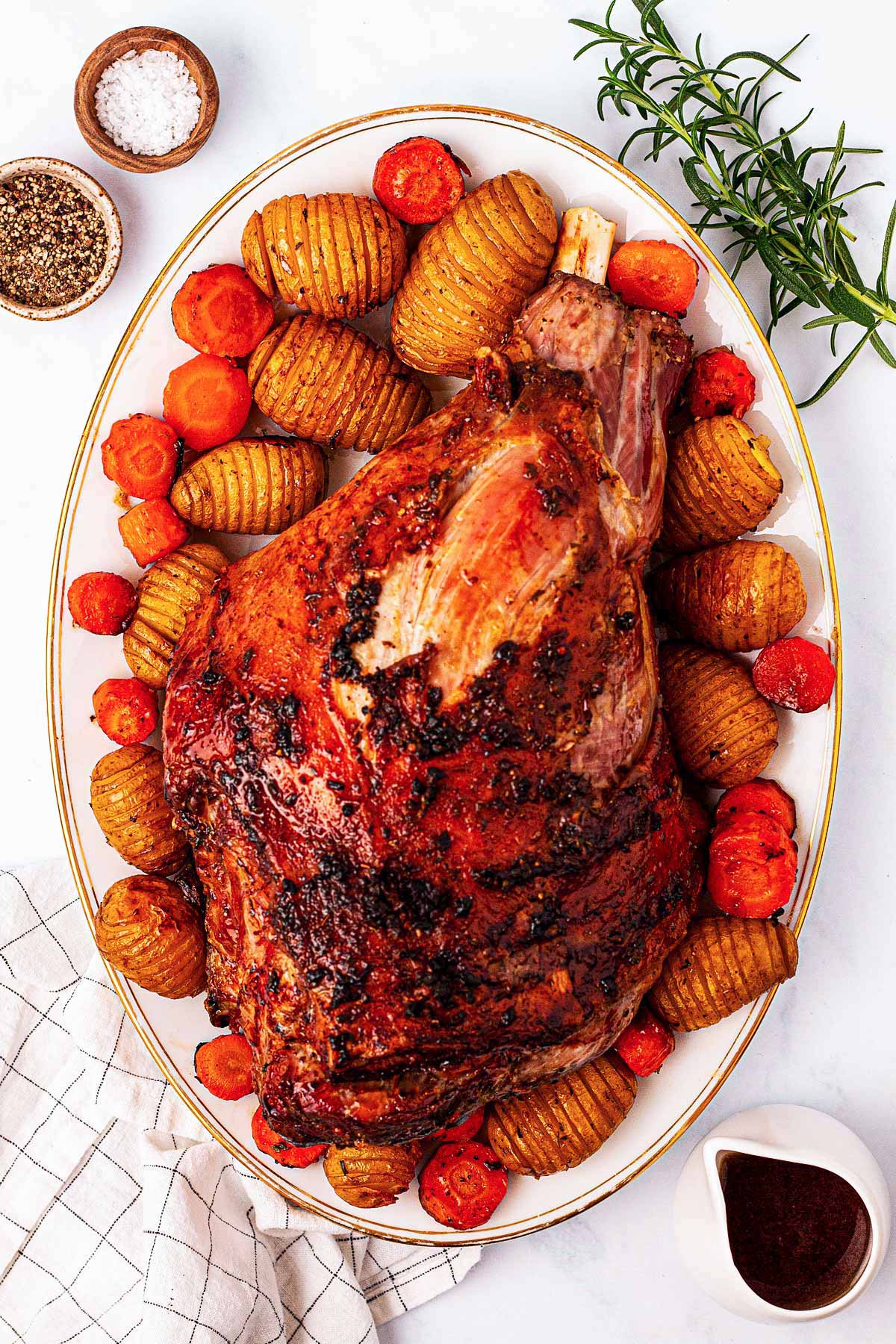 overhead view of roasted leg of lamb on platter with potatoes and carrots