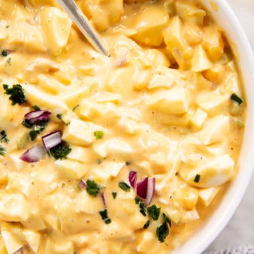 overhead close up view of egg salad topped with chives and red onion in white bowl