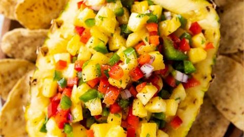 halved and hollowed out pineapple filled with pineapple salsa on a bed of corn chips