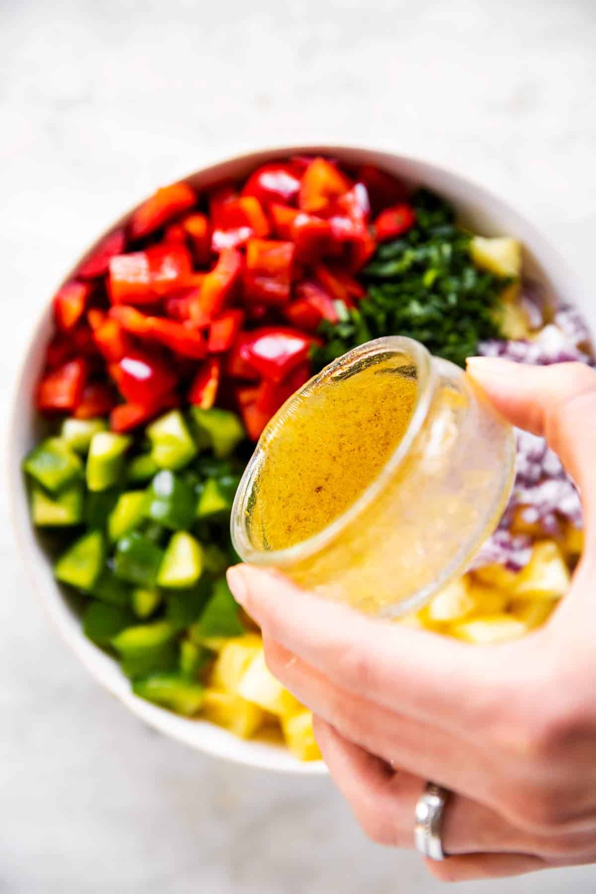 female hand pouring honey lime dressing over pineapple salsa ingredients