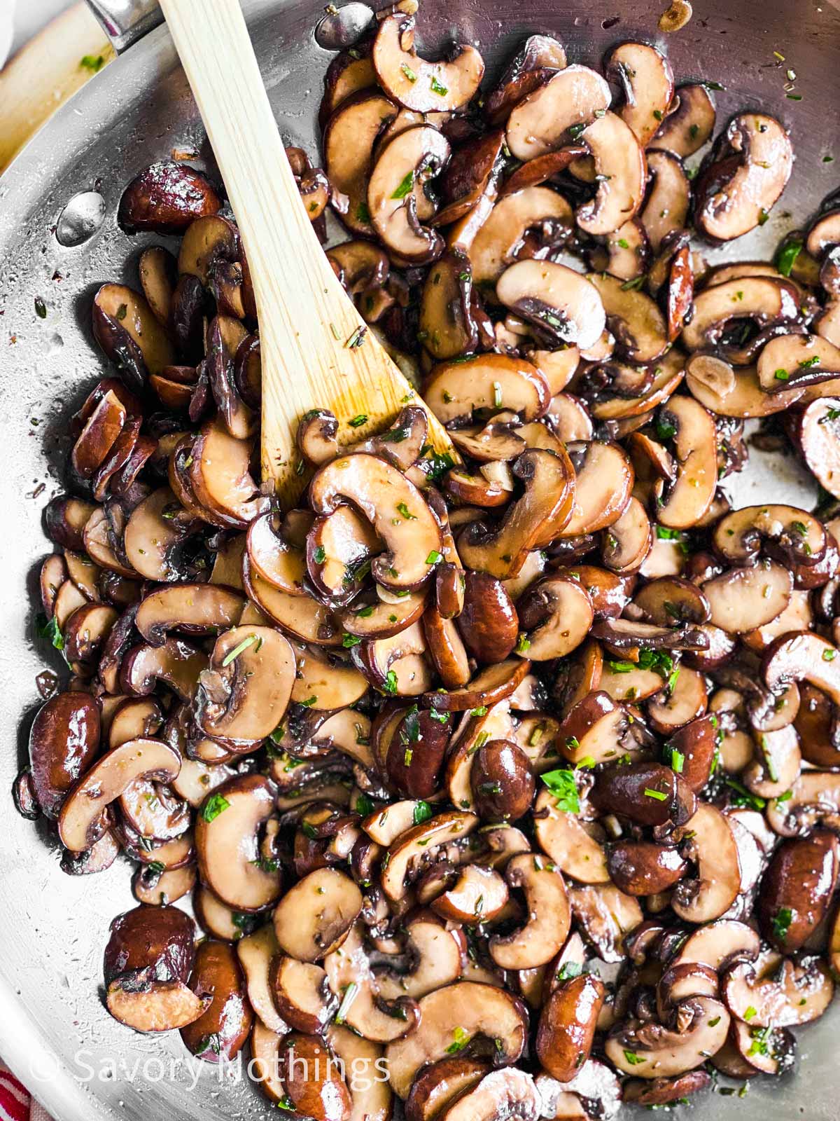 overhead view of sautéed mushrooms in skillet with wooden spoon