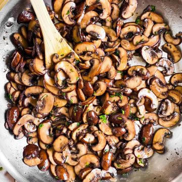 overhead view of sautéed mushrooms in skillet with wooden spoon