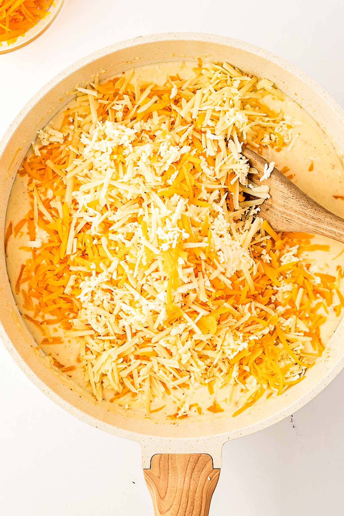 overhead view of shredded cheese and béchamel in skillet