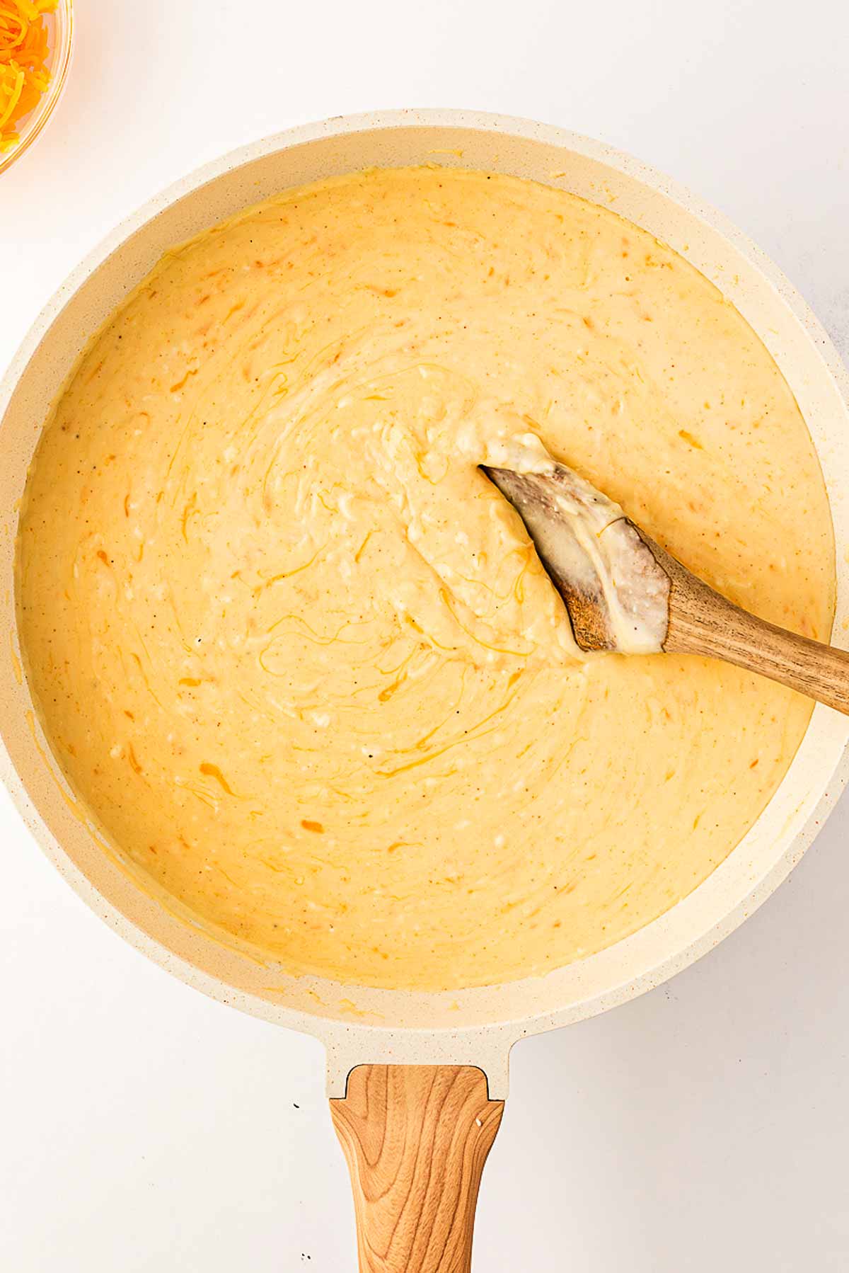 overhead view of cheese sauce in skillet being stirred with wooden spoon