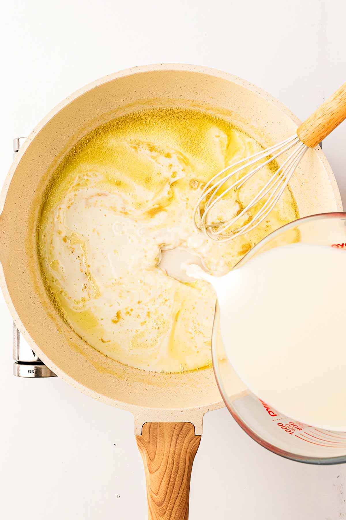 overhead view of milk being poured into roux in skillet