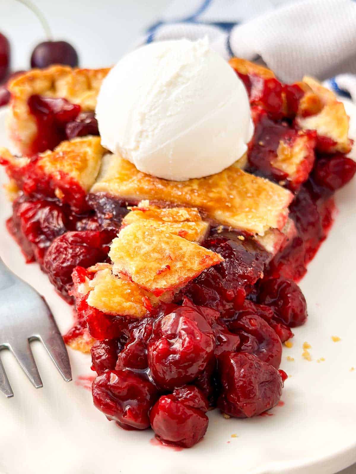 frontal close p view of cherry pie slice with a scoop of vanilla ice cream