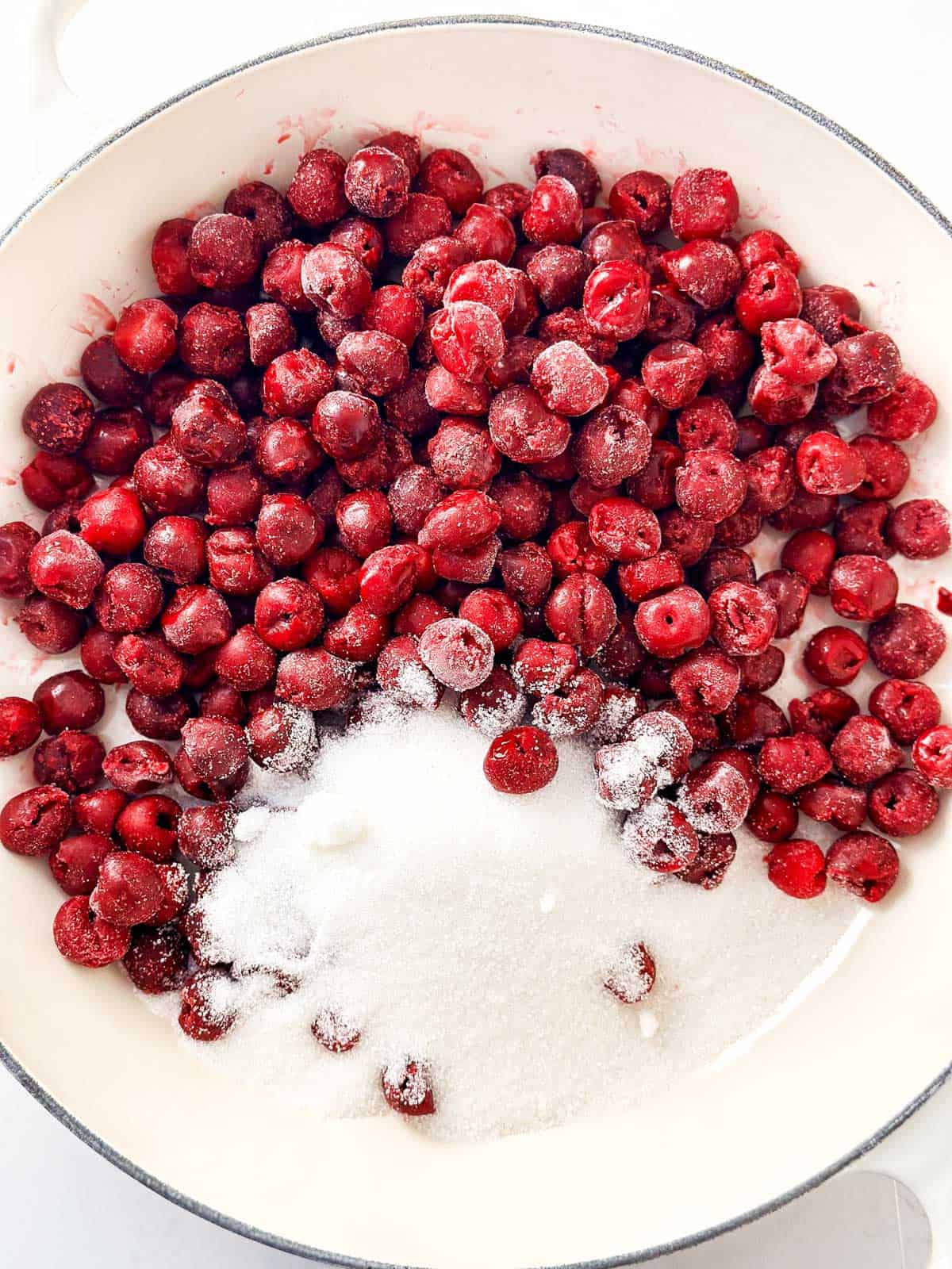 overhead view of frozen cherries and sugar in white skillet 