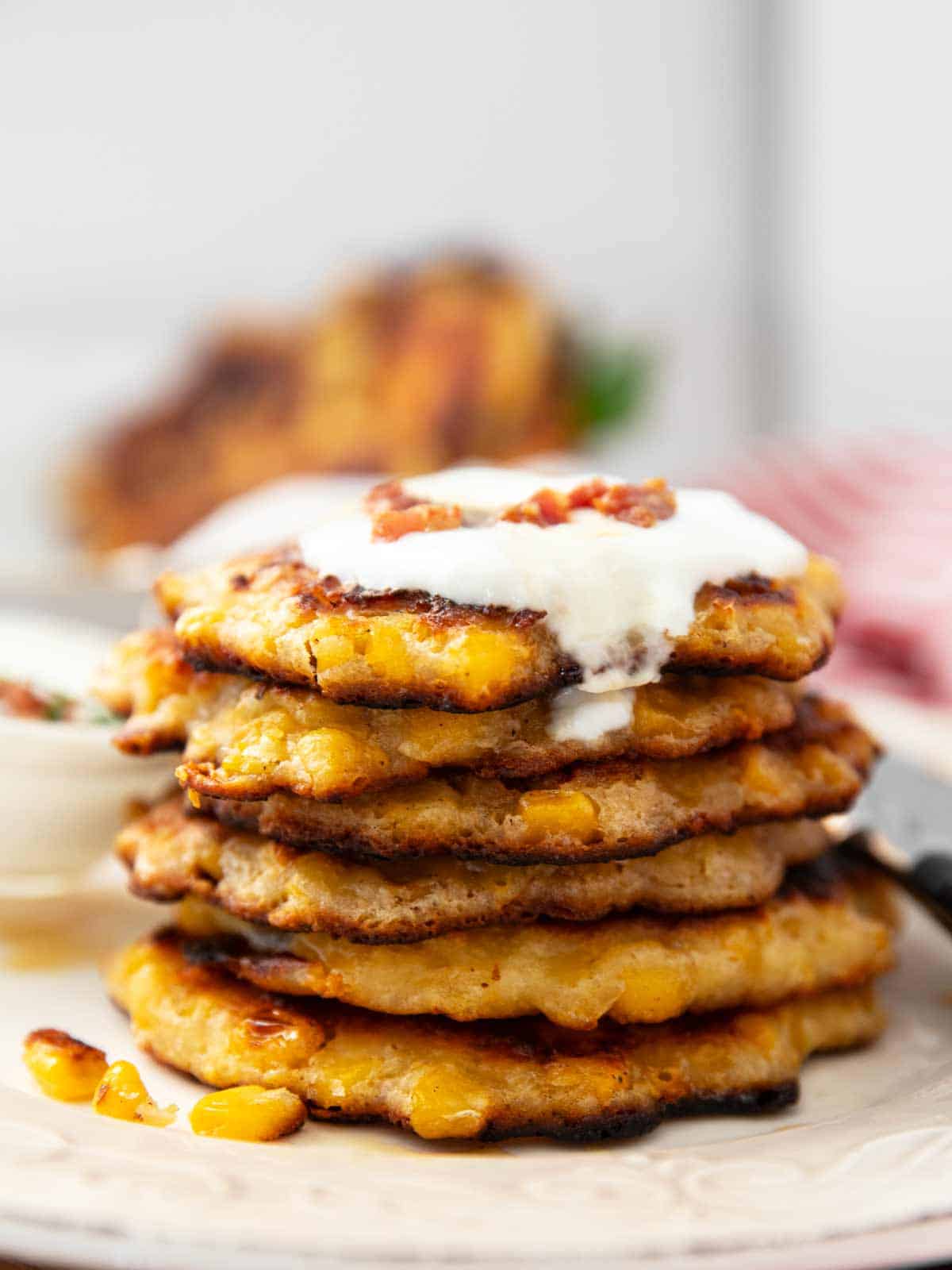 stack of corn fritters topped with sour cream and bacon