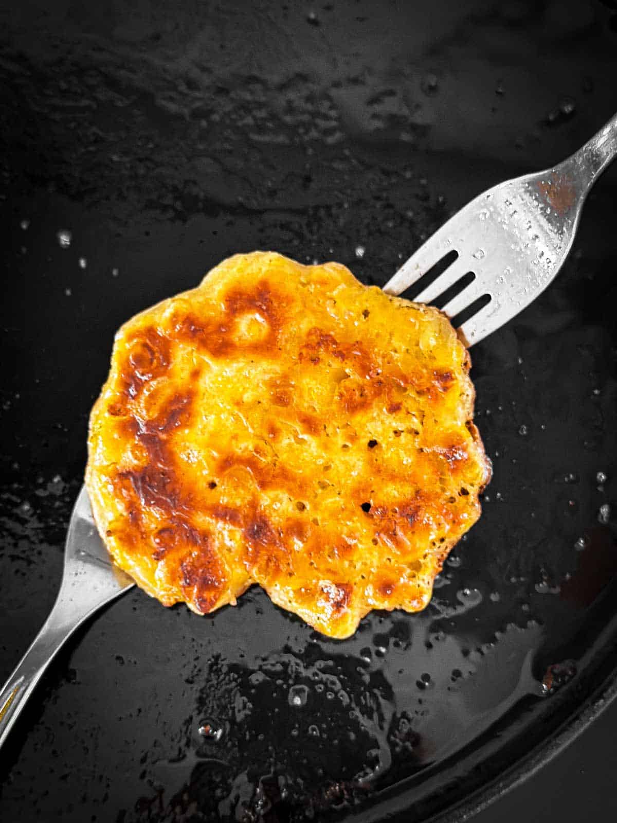 two forks flipping a corn fritter on griddle