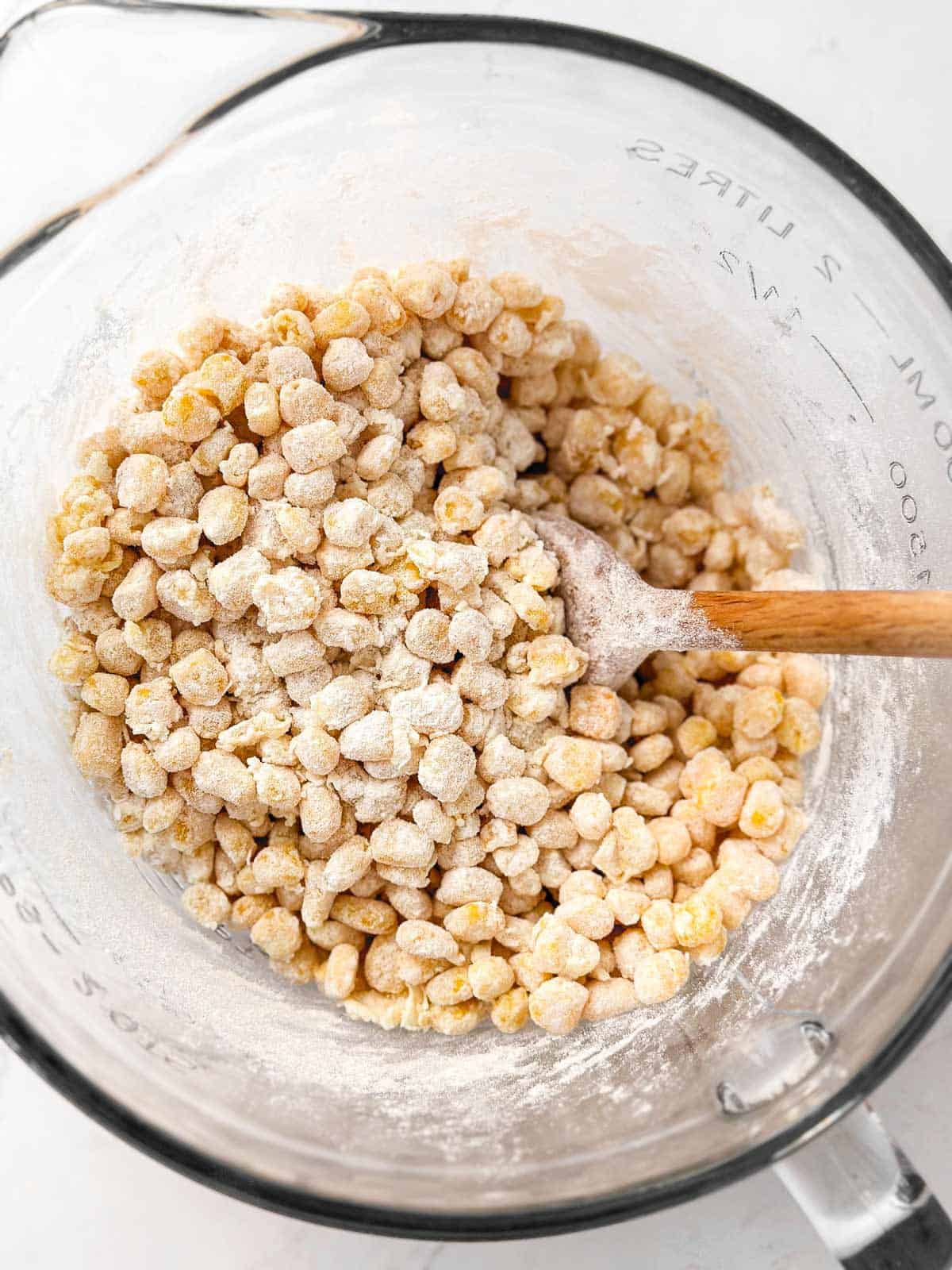 flour coated corn kernels in glass bowl with wooden spoon stuck in