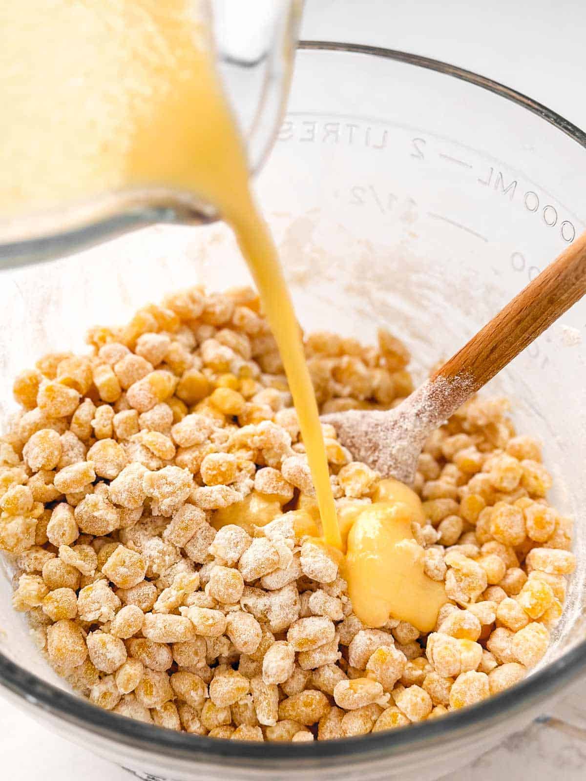 egg mixture pouring from glass measuring jug over flour coated corn kernels
