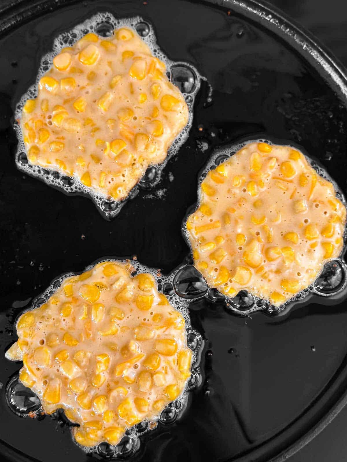 overhead view of three uncooked corn fritters on griddle surface