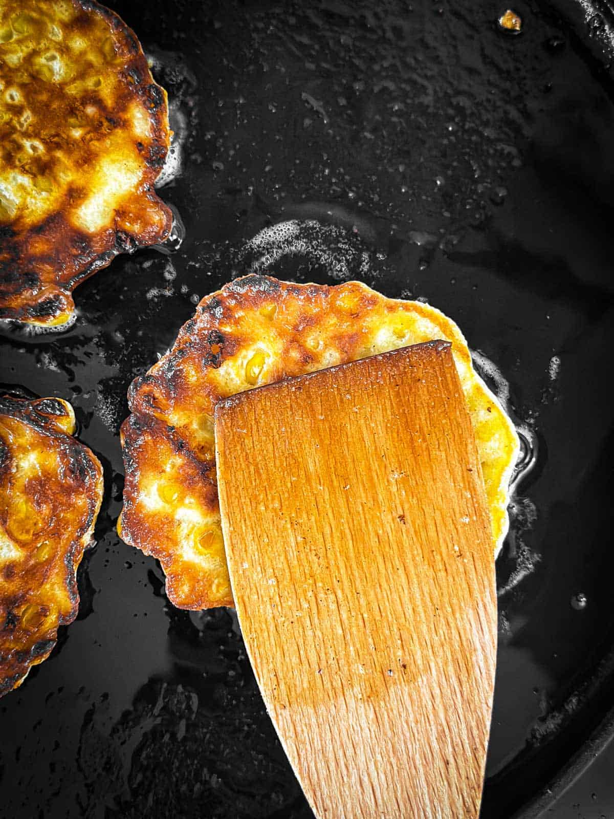 overhead view of wooden spatula pushing down on corn fritter on griddle