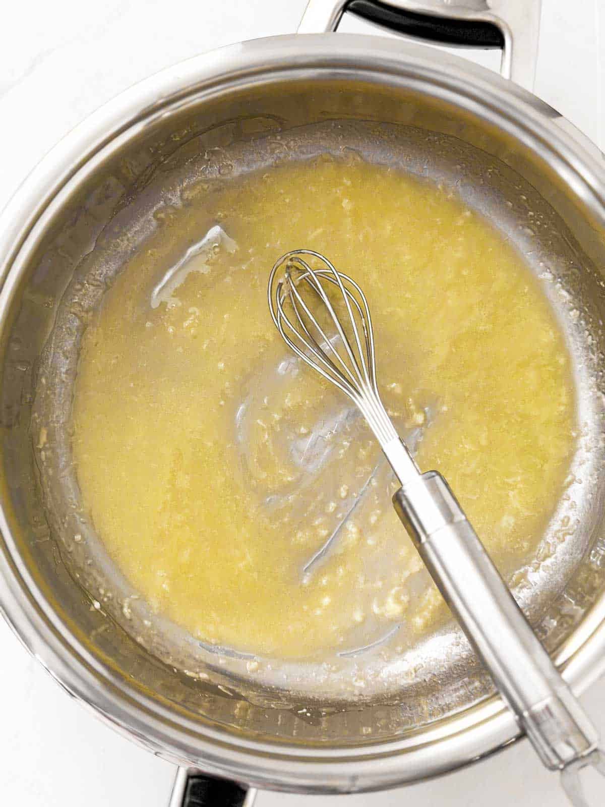 overhead view of garlic and flour cooked in butter in skillet with whisk