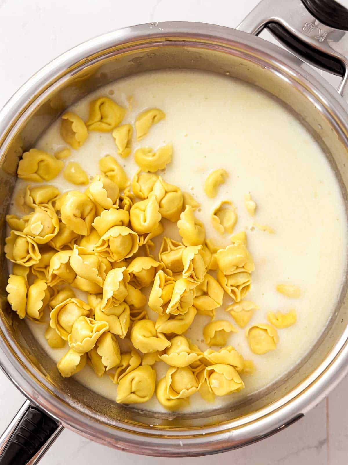 overhead view of uncooked tortellini in skillet with cream sauce