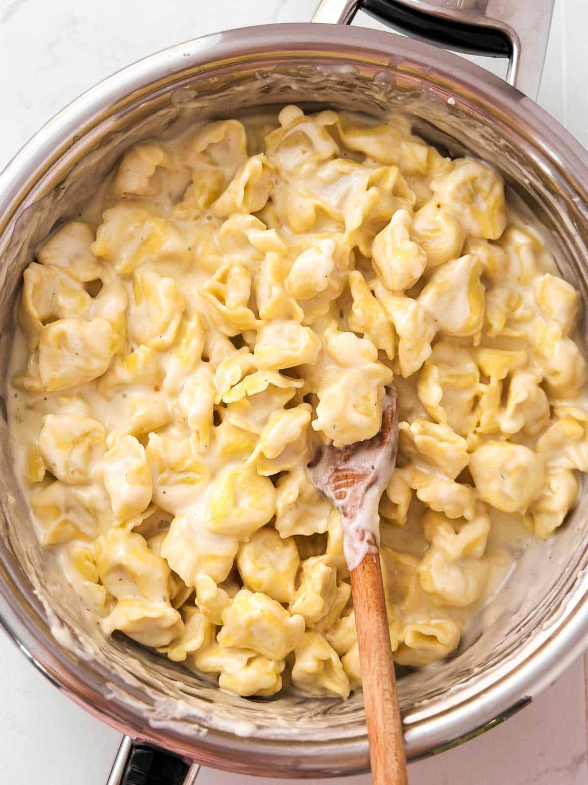 overhead view of garlic parmesan creamy cheese  tortellini in skillet with wooden spoon