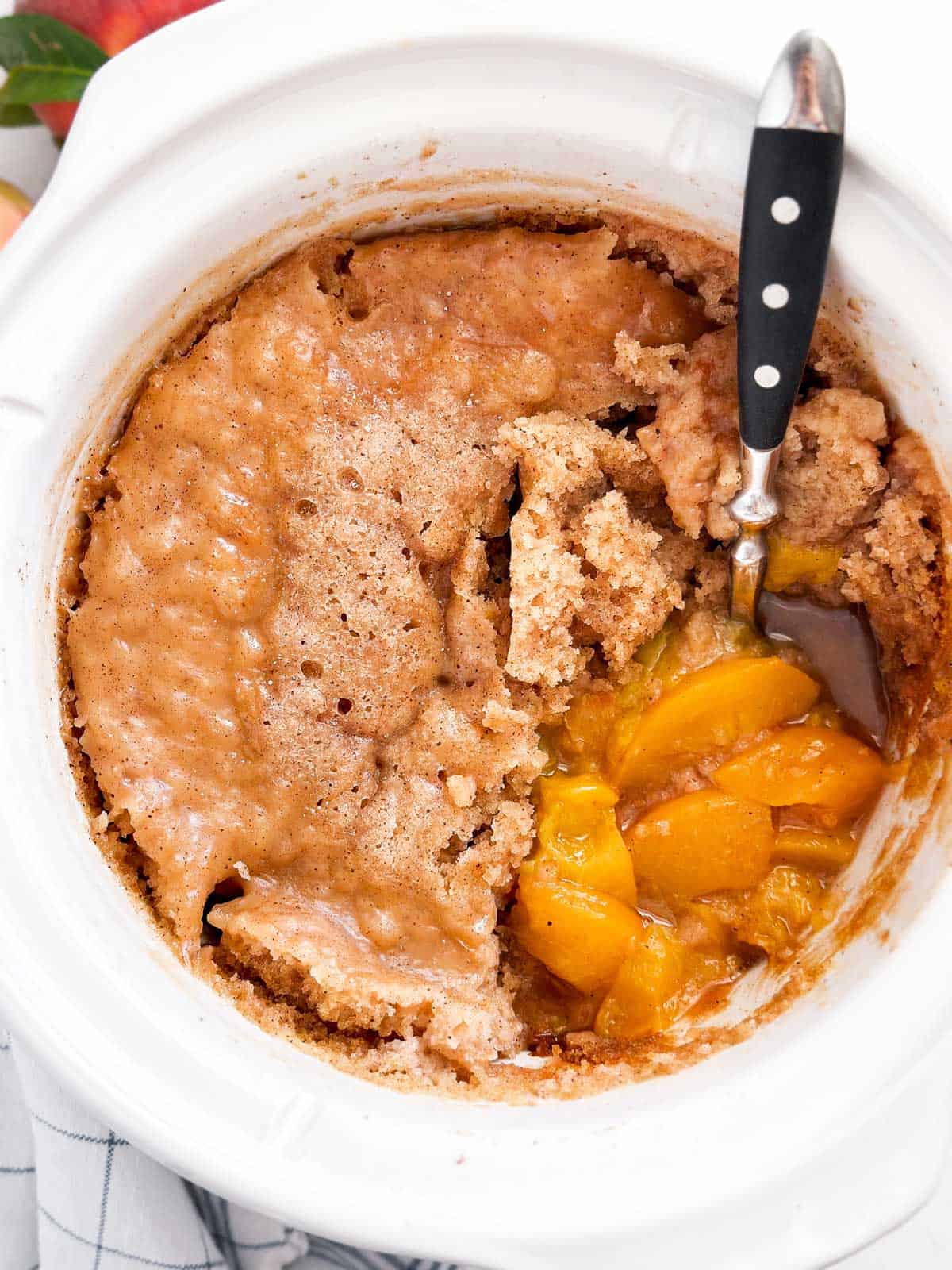 overhead view of peach cobbler in crockpot with spoon