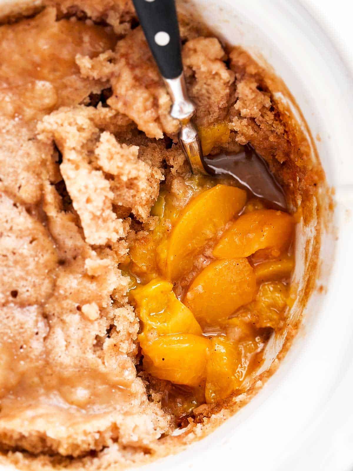 close up view of peach cobbler in white crock