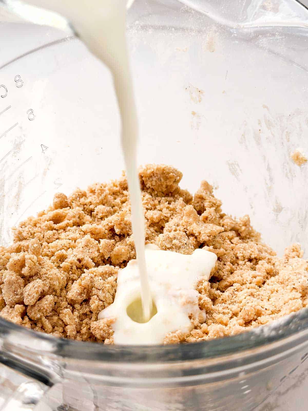 close up view of buttermilk pouring from glass jug over crumble mixture
