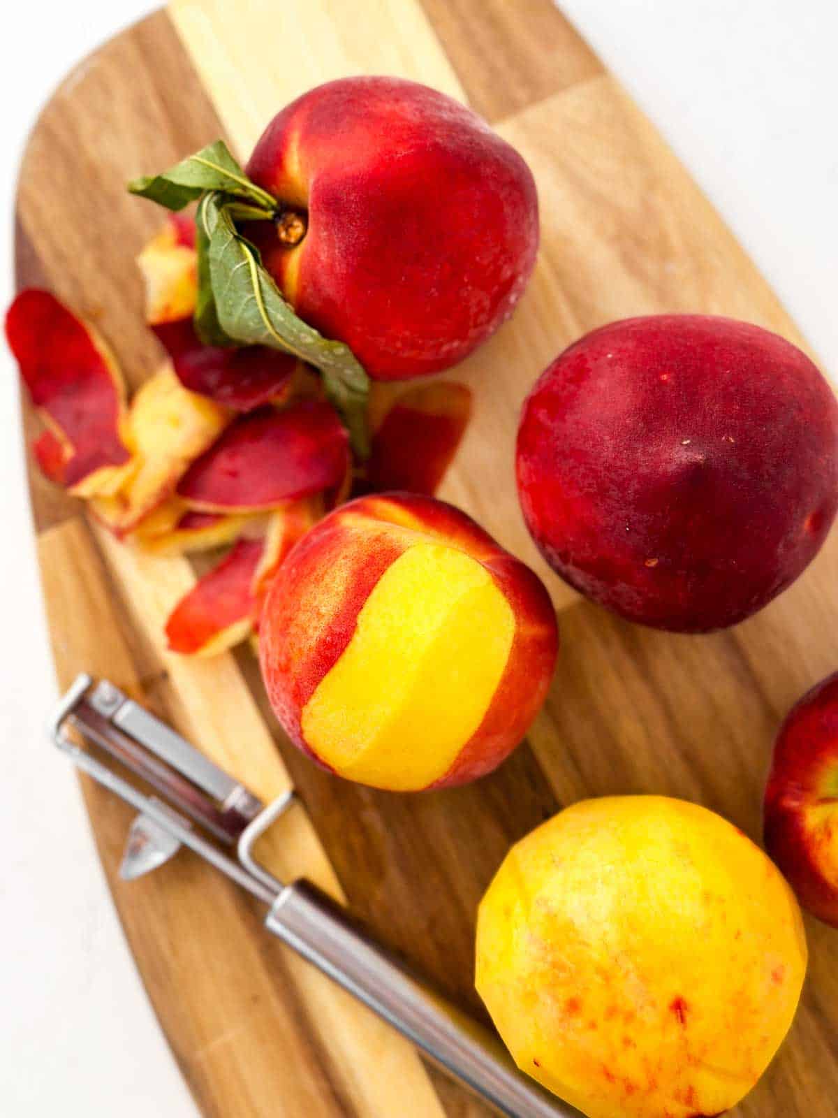 peaches with vegetable peeler on wooden chopping board