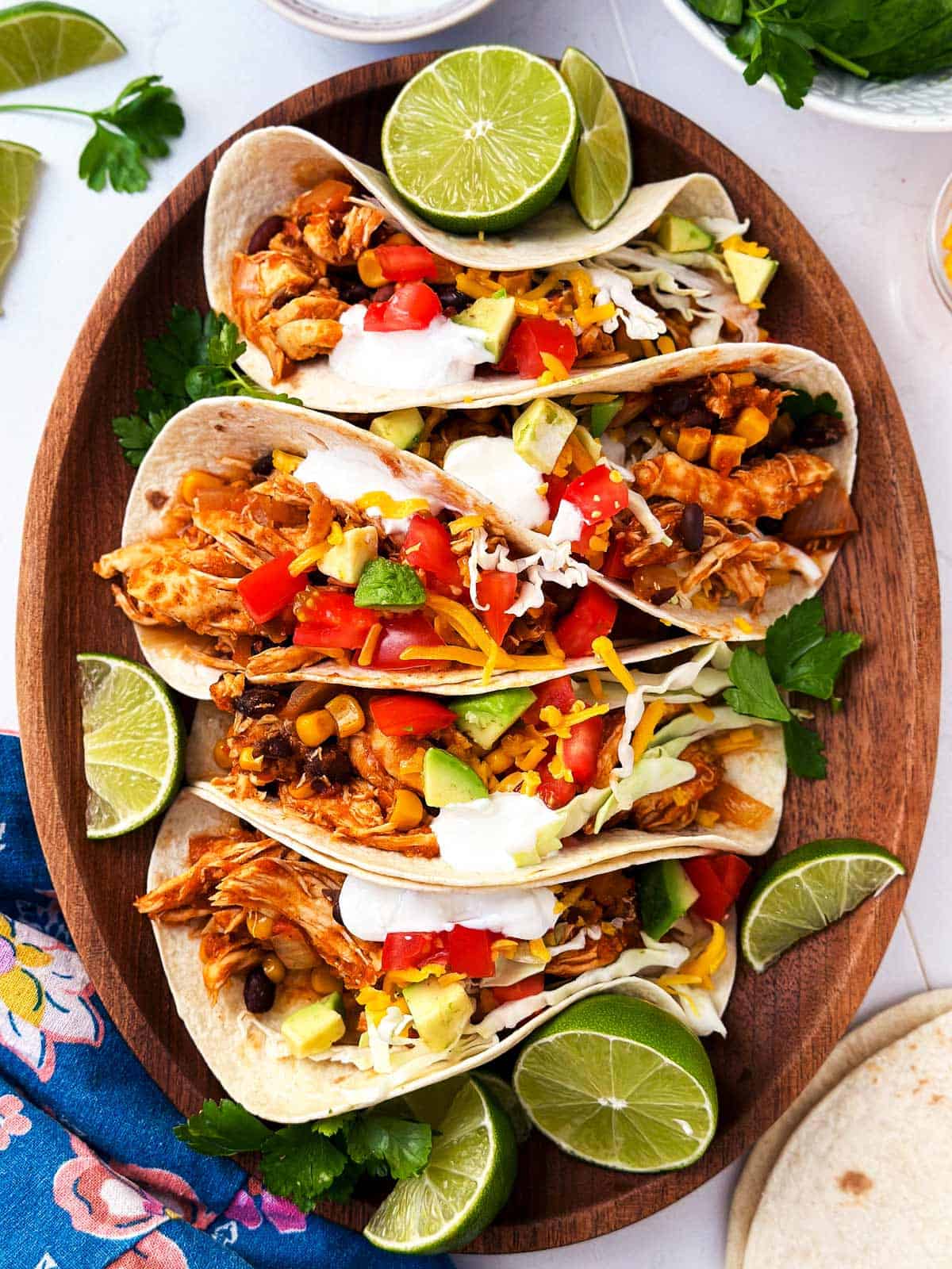 overhead view of five chicken tacos on wooden platter surrounded by taco toppings