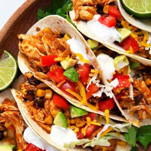 overhead close up view of crock pot chicken tacos with toppings on wooden platter