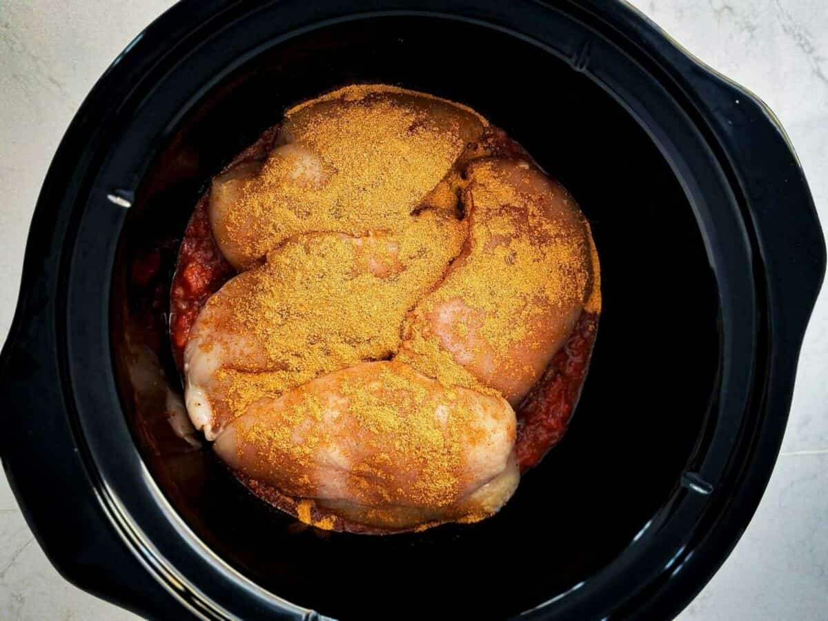 raw chicken with taco seasoning on top in crock