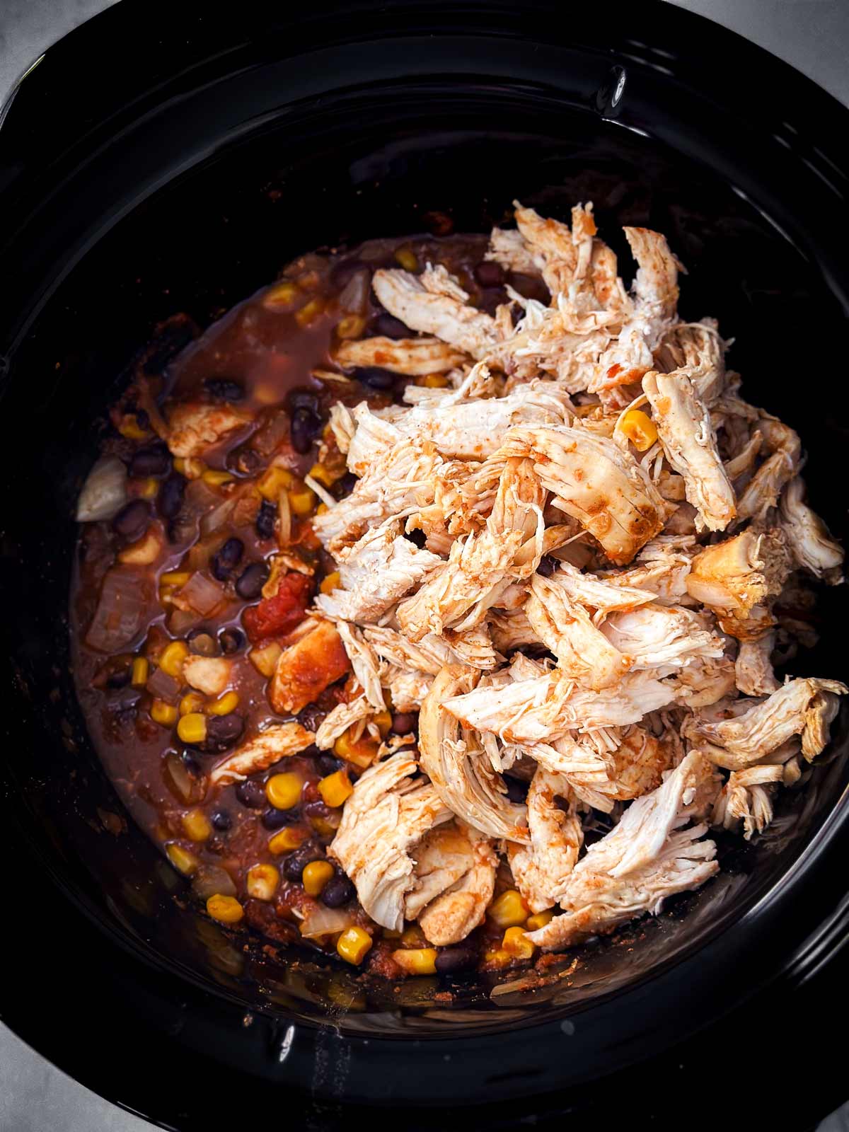overhead view of shredded chicken sitting on top of black bean and corn salsa in crock