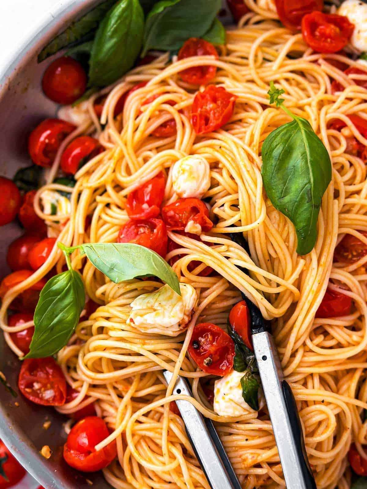 close up photo of kitchen tongs stuck in tomato basil pasta