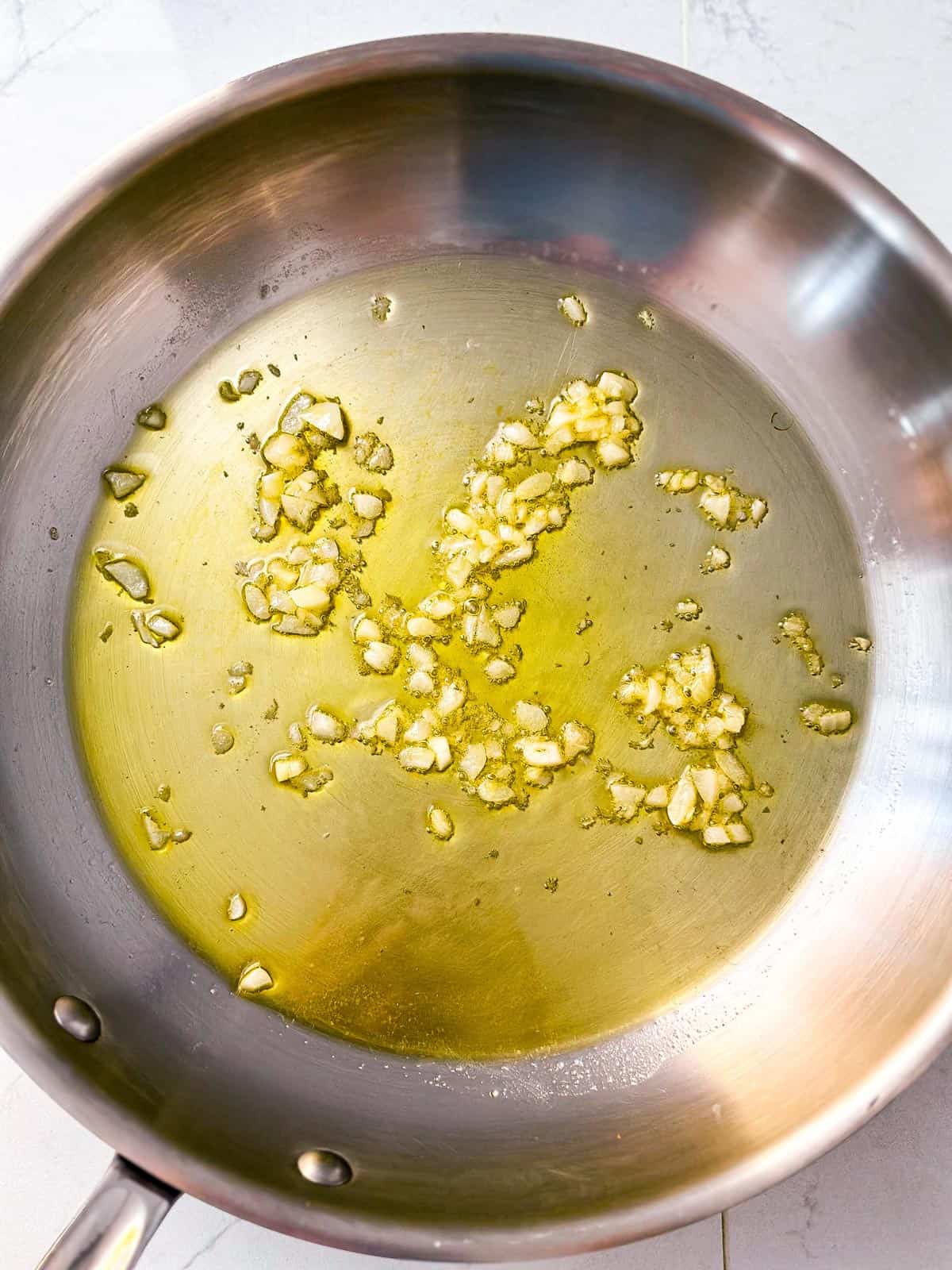overhead view of sautéed garlic in olive oil in skillet