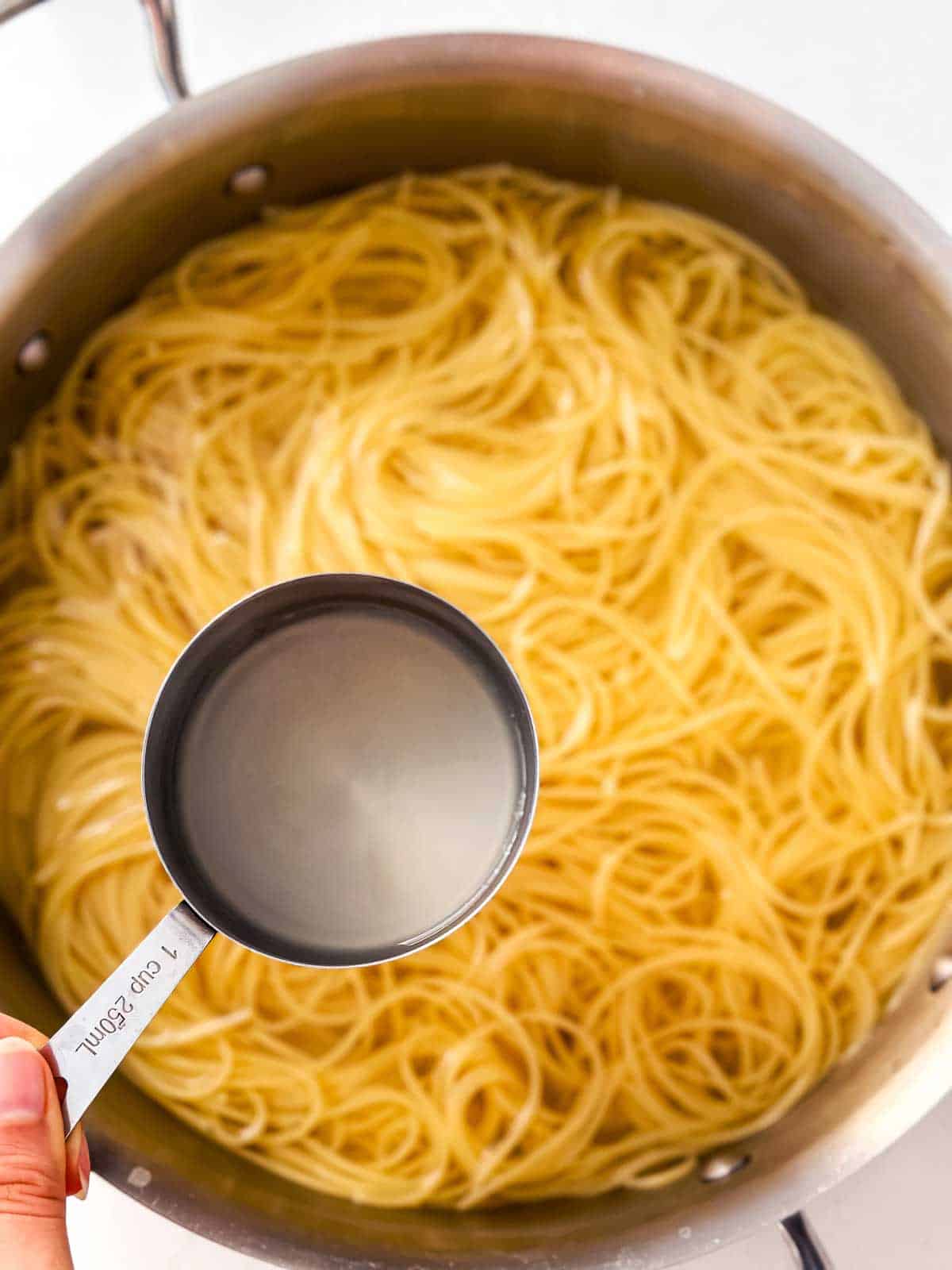 half cup measure held over pot of cooked spaghettini