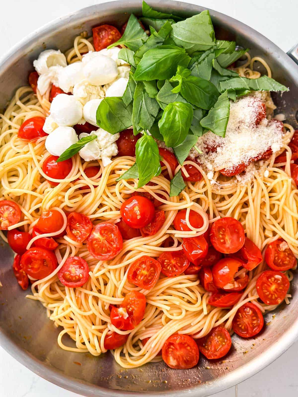 overhead view of spaghetti, tomatoes, mozzarella, basil and parmesan in skillet