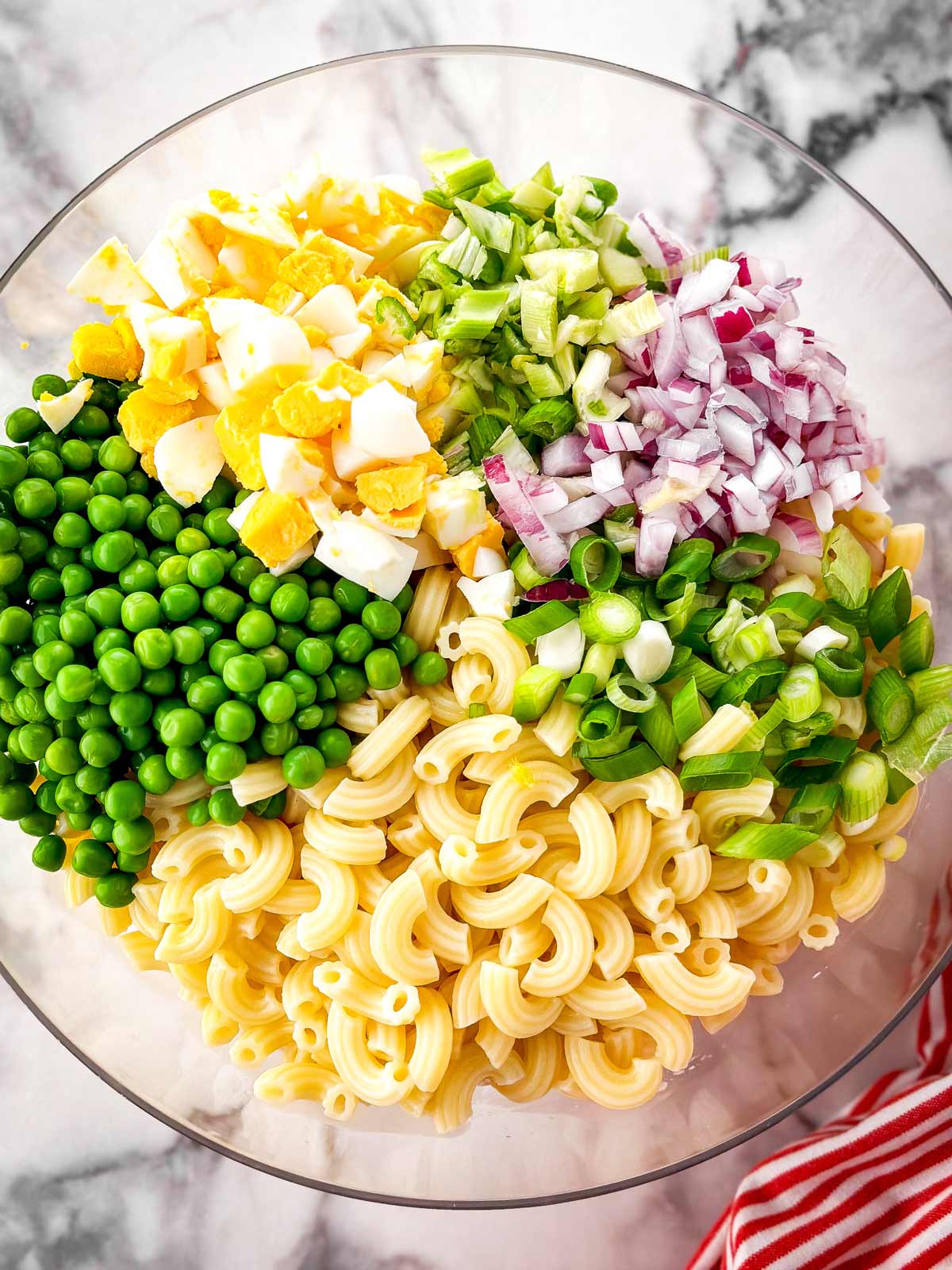 overhead view of ingredients for tuna macaroni salad in clear glass bowl