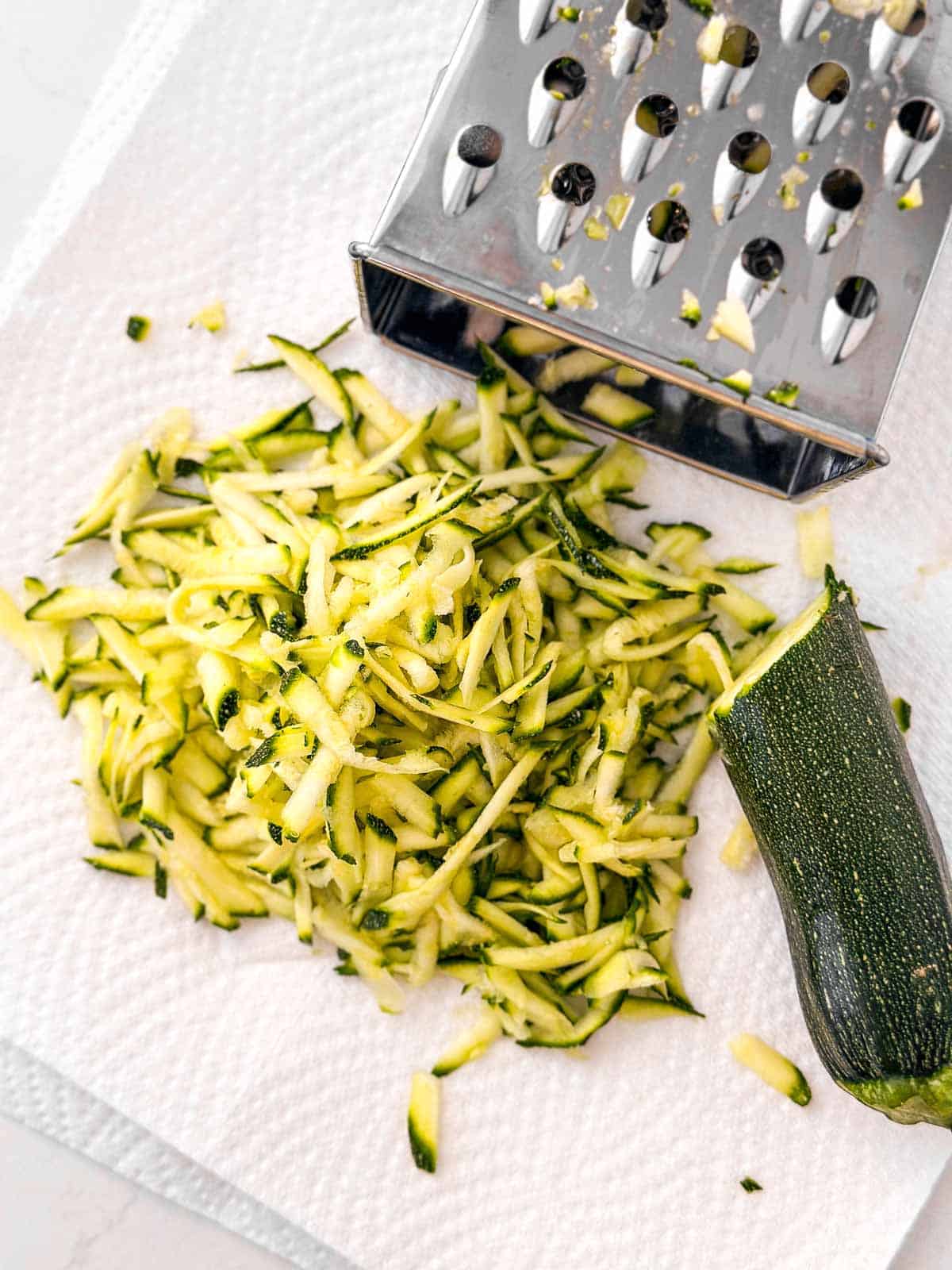 shredded zucchini on paper towel next to box grater