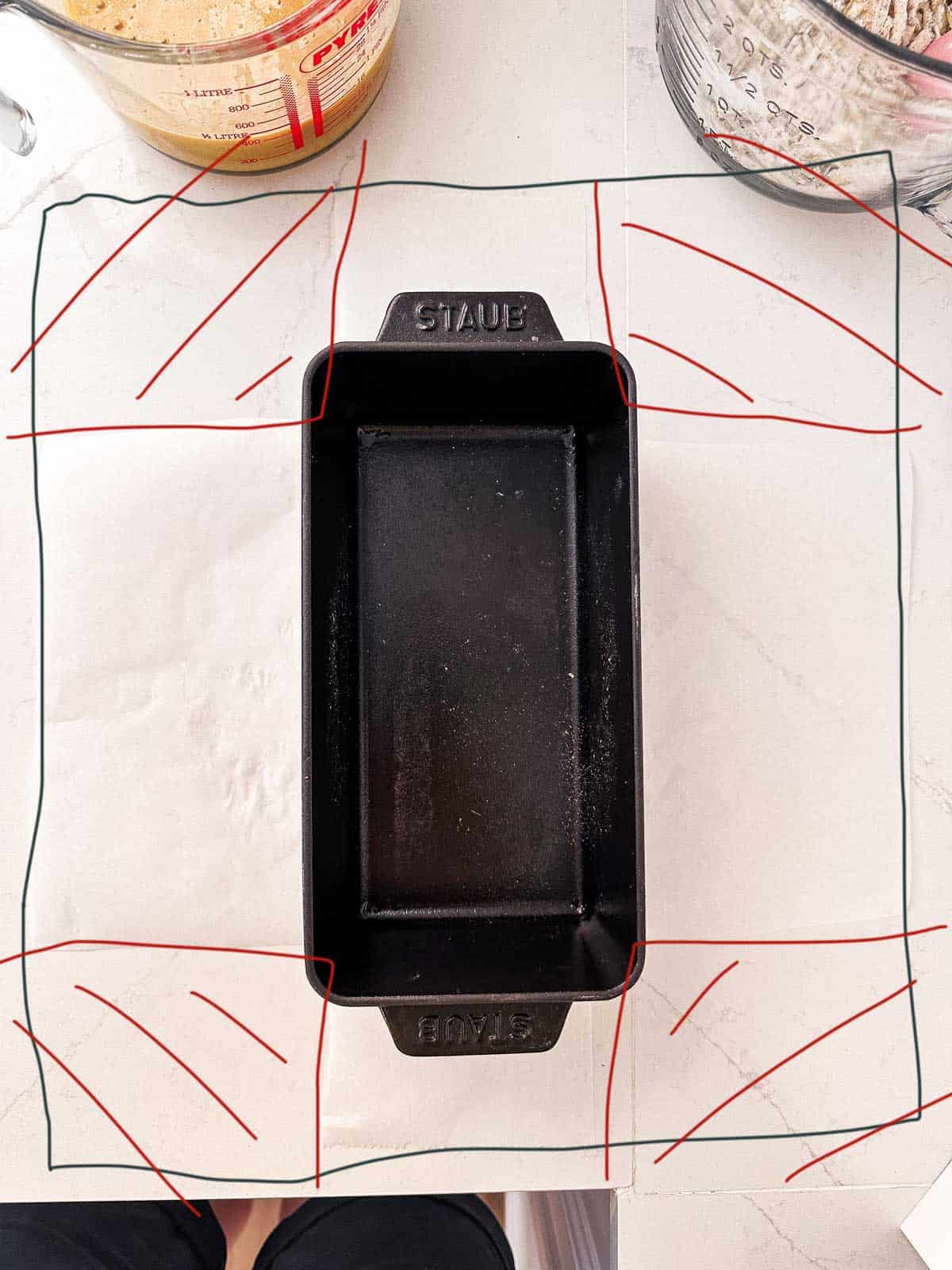 overhead view of loaf pan sitting on baking parchment, with drawing to show how to cut paper