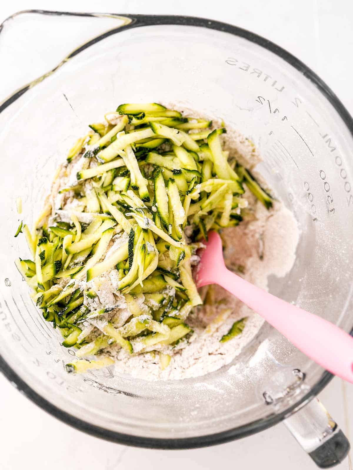 overhead view of shredded zucchini sitting on top of flour mixture in glass bowl