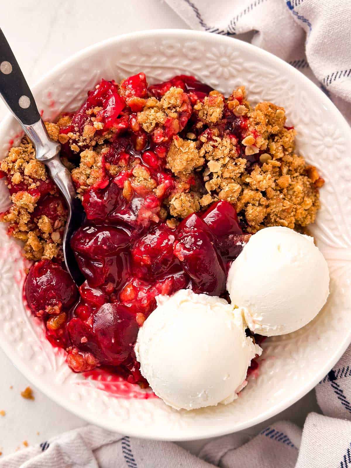 overhead view of cherry crisp in white bowl with two scoops vanilla ice cream