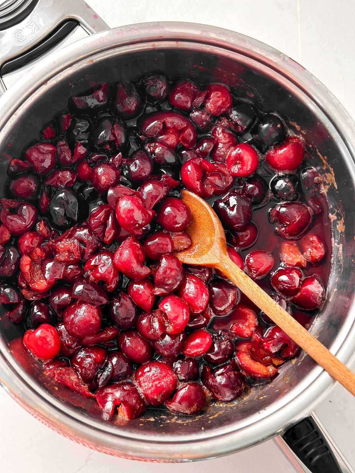 overhead view of cooked cherries in pan with wooden spoon