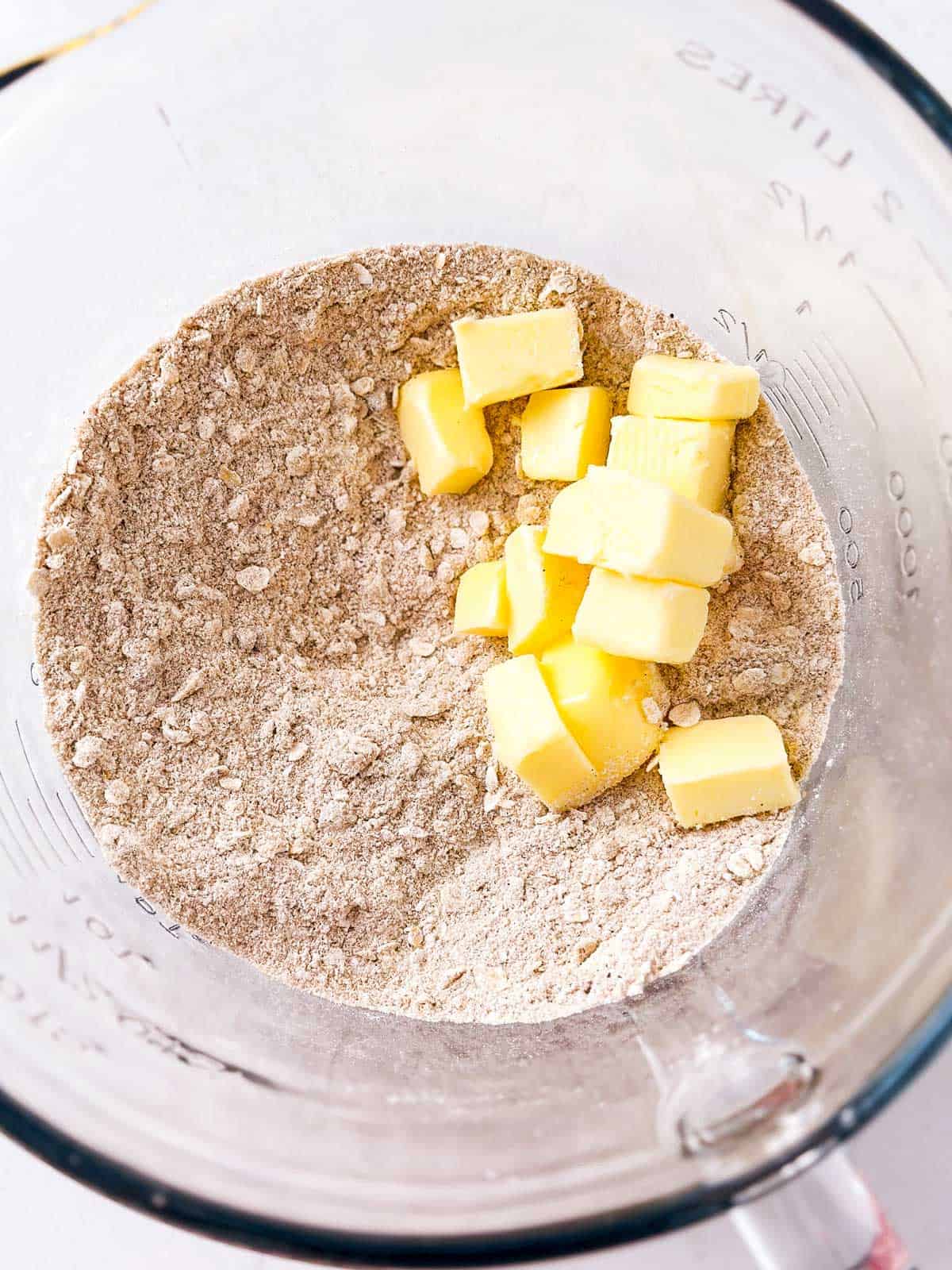 overhead view of dry ingredients for crumble topping in glass bowl with butter