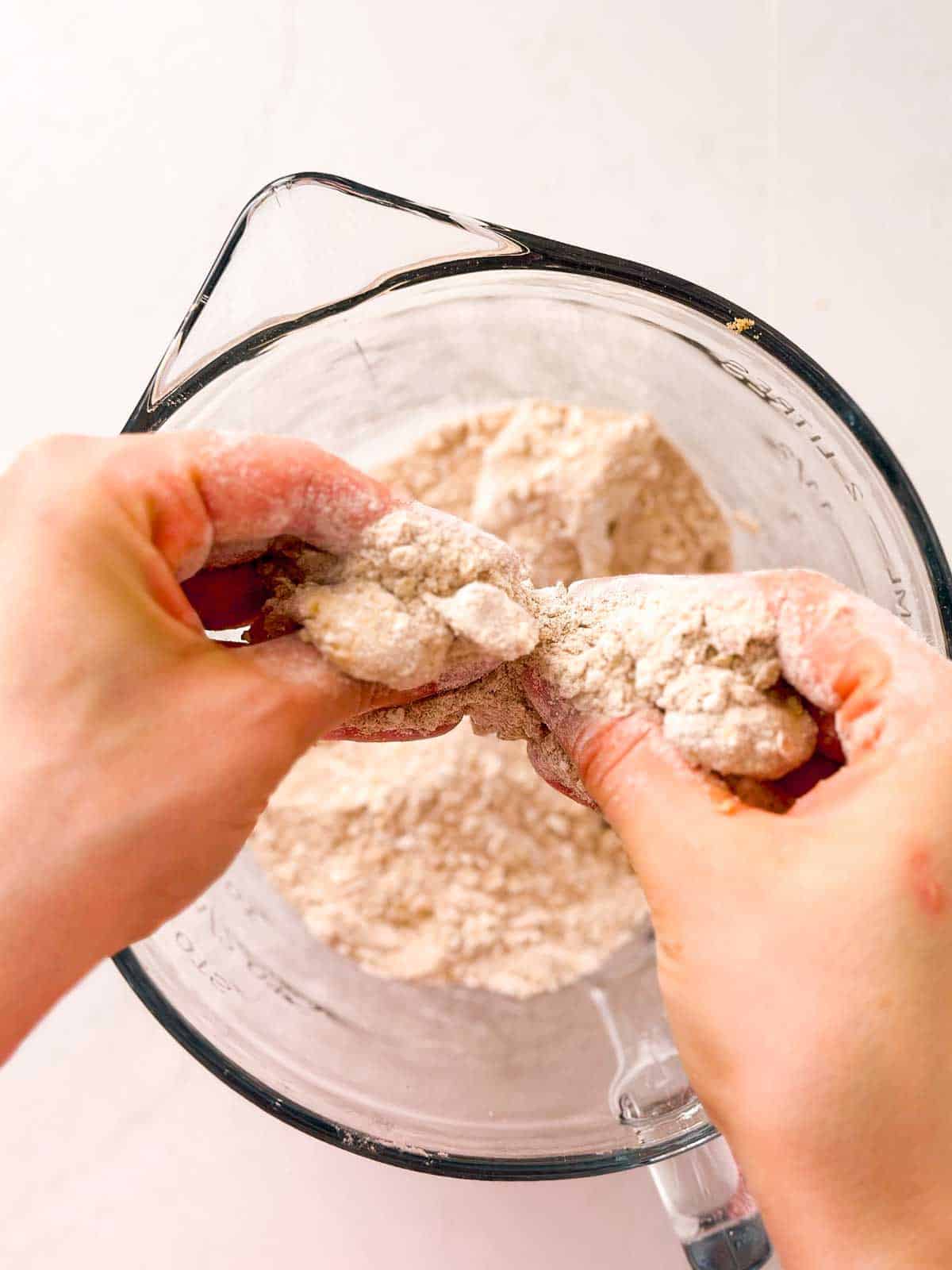 overhead view of female hands grabbing crumble topping mixture from glass bowl