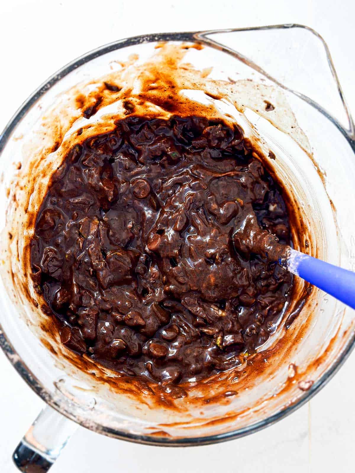 overhead view of chocolate zucchini bread batter in glass bowl with blue spatula stuck in